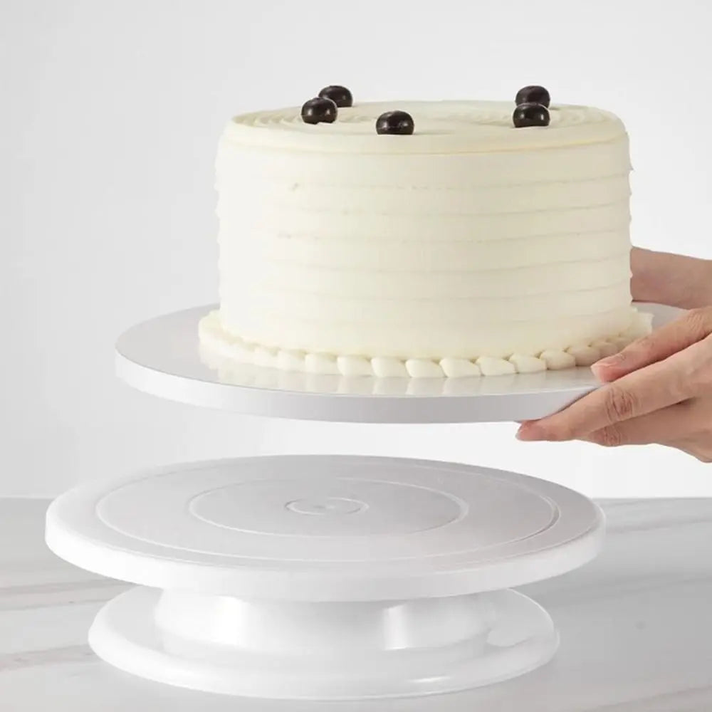 A white layer cake with dark berries on top displayed on a white cake board.