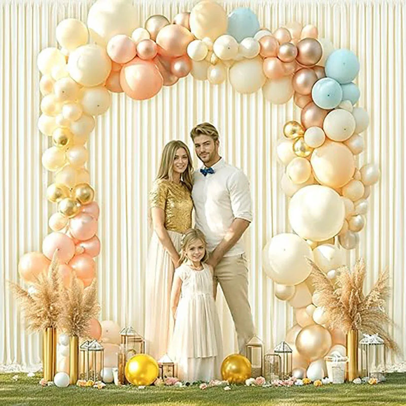 A floral arch made of light pink, cream, and gold balloons decorated with dried pampas grass and a couple.