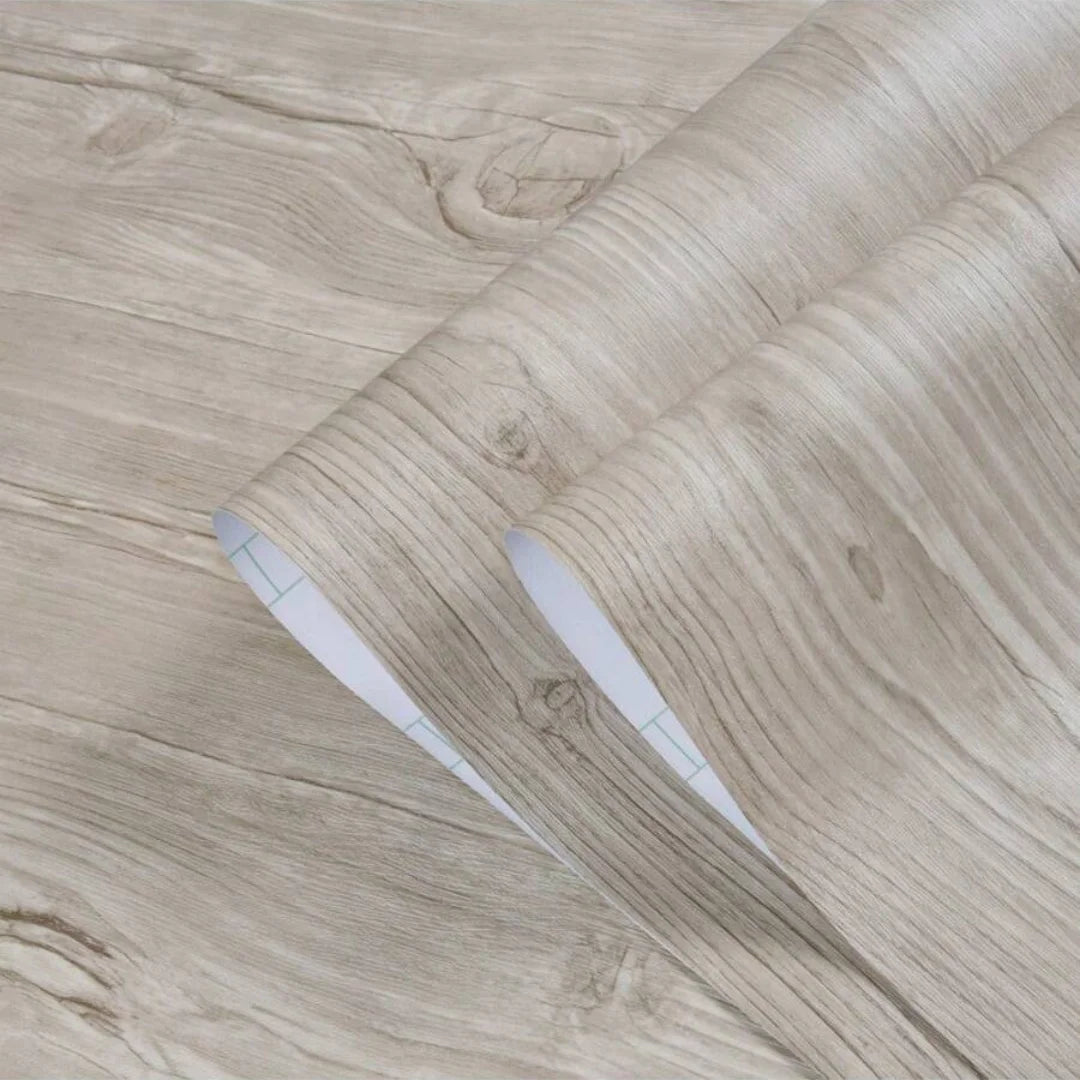 Roll of self-adhesive PVC wallpaper film with a wood grain texture shown rolled up on a wooden surface.