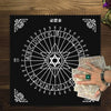 A black cloth featuring a pentagram tarot wheel design with letters and numbers, displayed on a wooden surface.