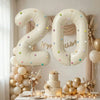 Two large milky white aluminum foil number balloons 2 and 0 decorated with gold and white balloons and floral arrangements