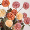 A bouquet of artificial chrysanthemum pompon flowers in shades of peach, orange, and pink on dark green stems.