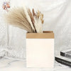 A bouquet of dried pampas grass and other grasses in a light brown paper box against a white lace background.