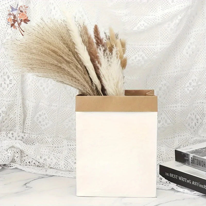 A bouquet of dried pampas grass and other grasses in a light brown paper box against a white lace background.