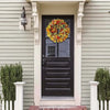 A black door with a wreath of colorful artificial flowers is centered in a light gray door frame.