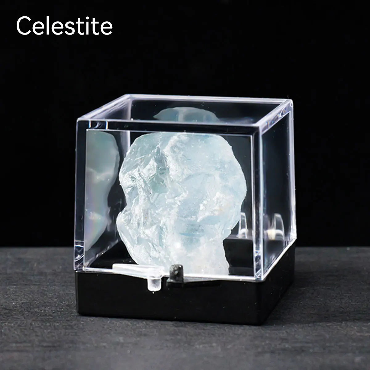 A clear Celestite crystal specimen is displayed inside a black glass box on a dark surface.