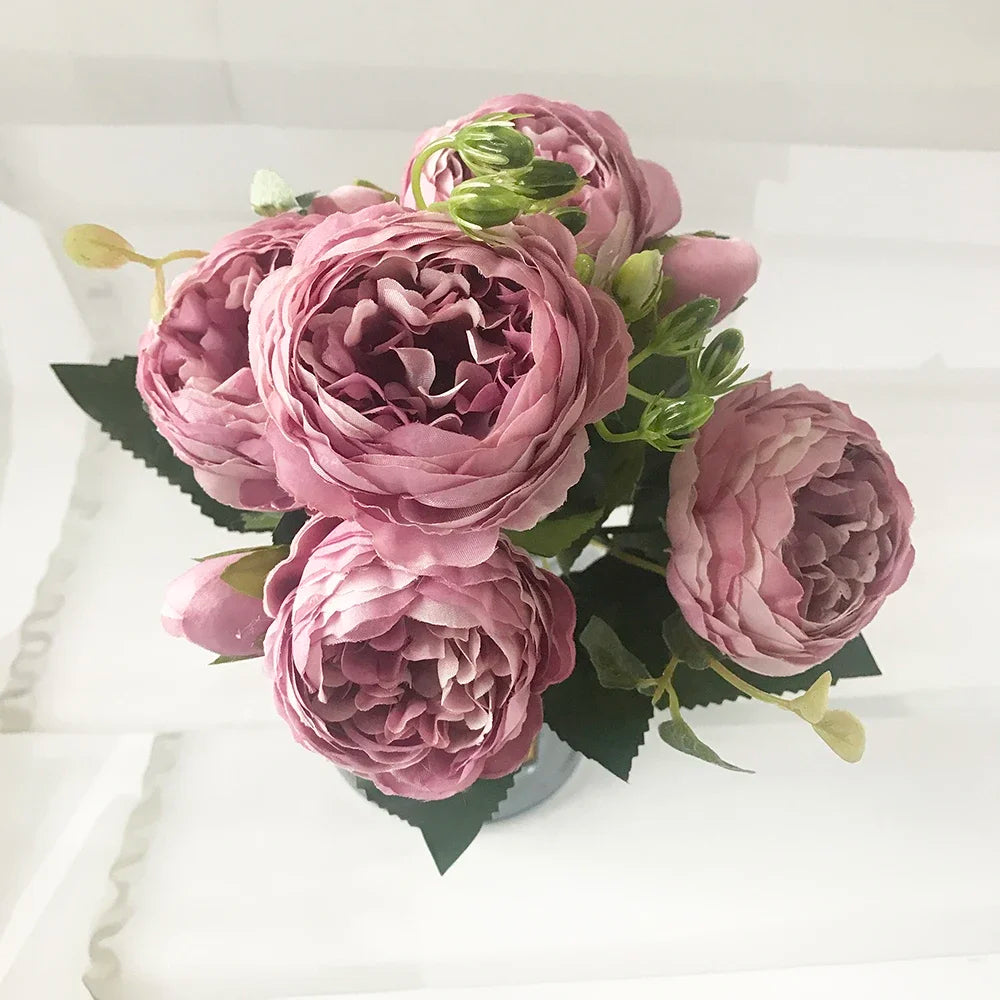 A bouquet of pink and mauve silk rose and peony artificial flowers with green leaves.