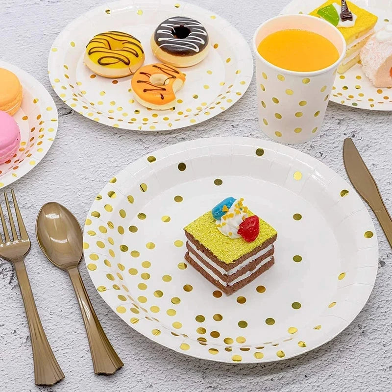 A white plate with gold polka dots holds a slice of cake decorated with colorful frosting and fruit, next to a yellow drink i
