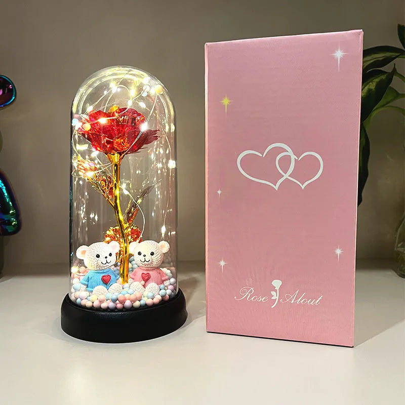 Una caja rosa con diseño de corazón junto a un vaso de exhibición con una rosa roja y ositos de peluche pequeños.