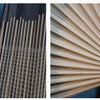 Close-up of a handwoven bamboo wall fan with light beige slats and a black tassel.
