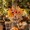 A decorative plastic pumpkin door hanger set is displayed on a wooden post surrounded by autumn foliage.