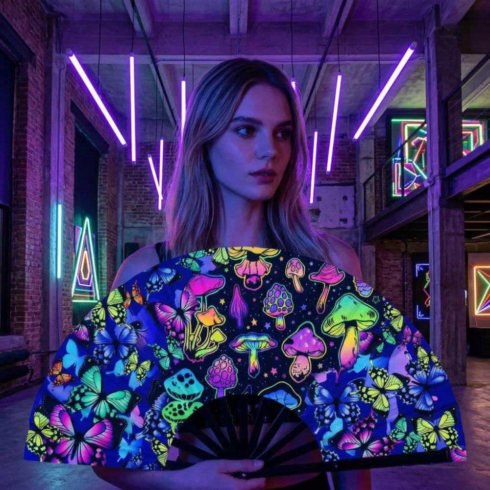 A woman holds a folding rave hand fan with a vibrant, fluorescent UV glow pattern featuring colorful mushrooms and butterflie