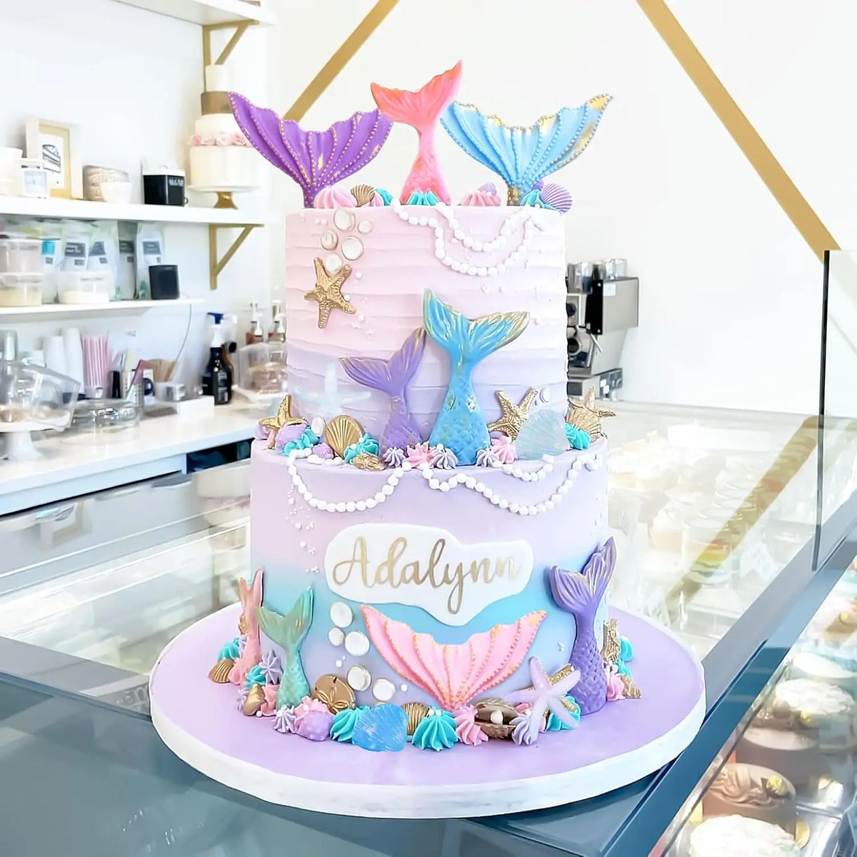 A tiered cake decorated in purple and blue mermaid tail shapes, seashells, and sea stars.