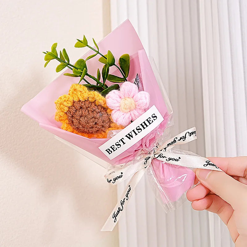 A pink paper bouquet featuring handmade crochet flowers in yellow and pink hues with a decorative ribbon