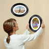 A woman is holding an oval picture frame with a view of the Eiffel Tower on a light-colored wall.
