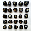 Una colección de piedras rúnicas de cristal natural en negro y oro dispuestas en una cuadrícula.