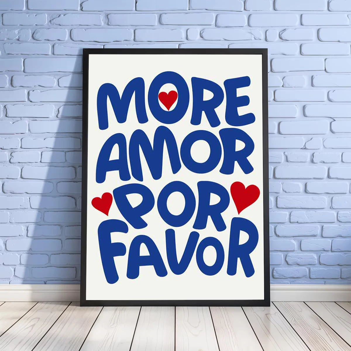 A framed canvas print featuring the text MORE AMOR POR FAVOR in bold blue letters with red hearts on a white background.