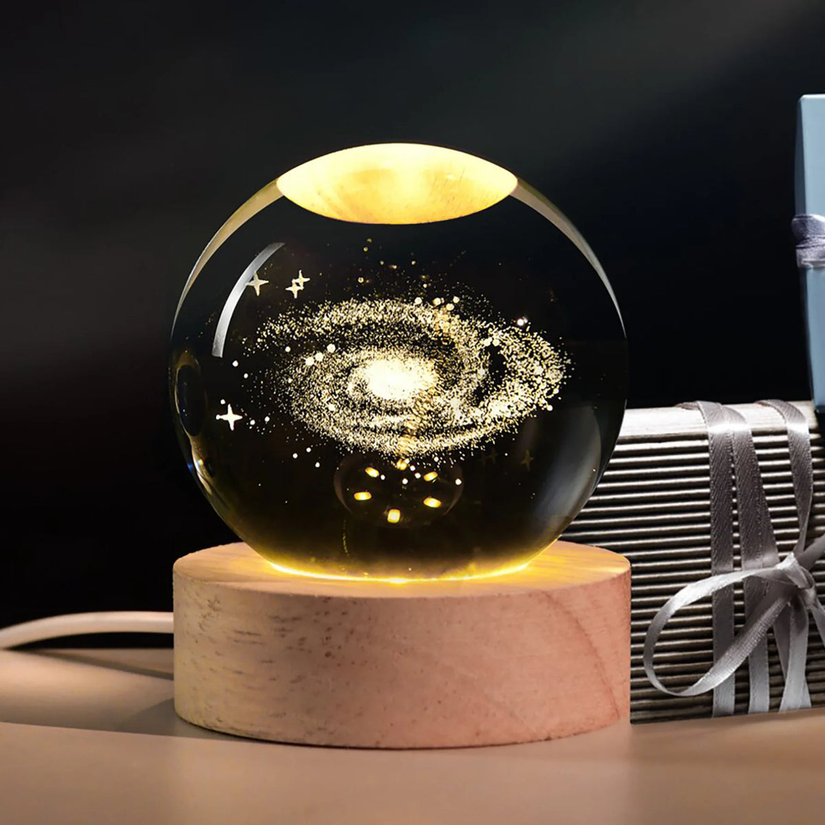 Galaxy crystal ball night light with a golden glow resting on a wooden base.
