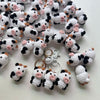 A collection of handmade crochet cow keychains in white and black with pink accents.