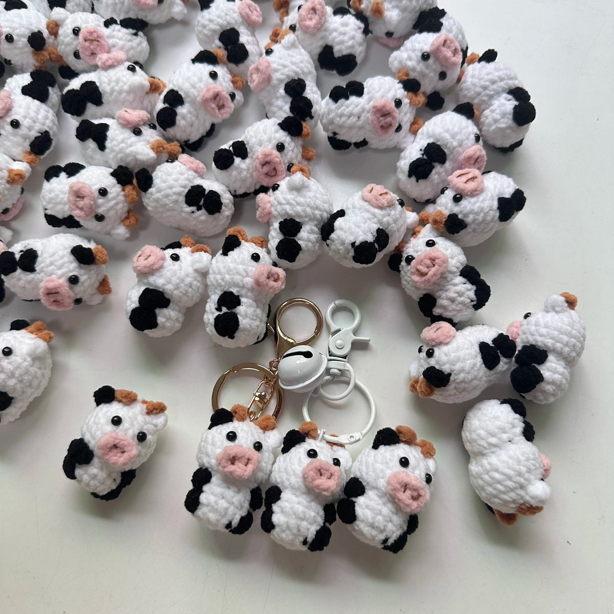 A collection of handmade crochet cow keychains in white and black with pink accents.