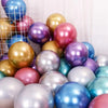 A collection of chrome metallic balloons in various shades of gold, purple, pink, and silver are displayed against a white ba