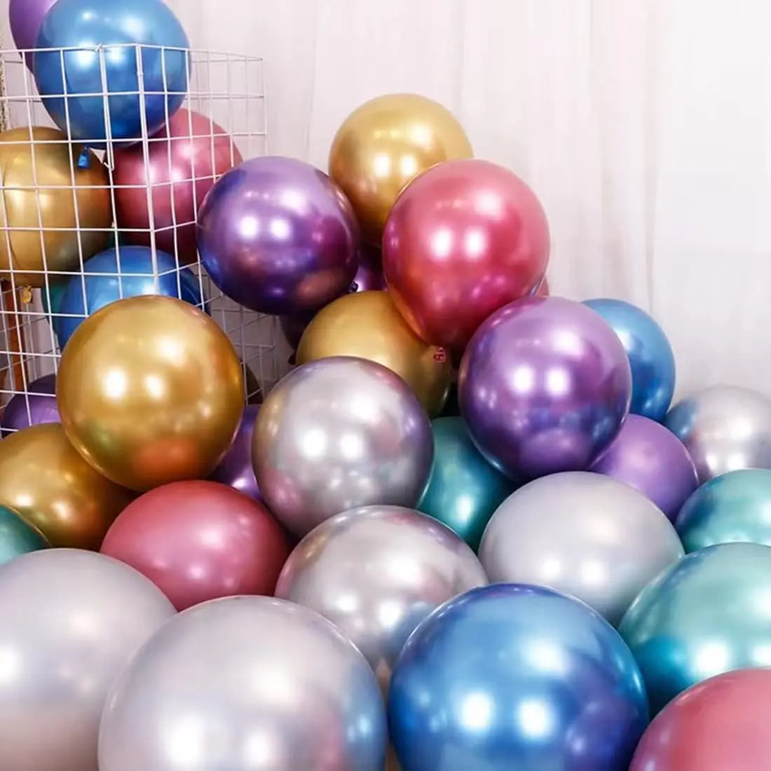 A collection of chrome metallic balloons in various shades of gold, purple, pink, and silver are displayed against a white ba