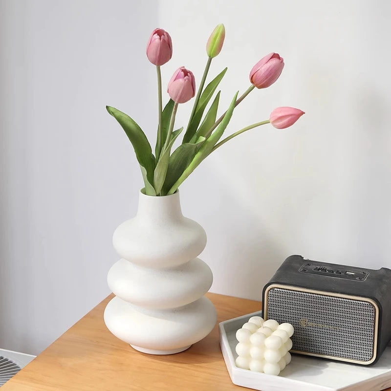 A white ceramic vase holds several pink tulips against a light background.