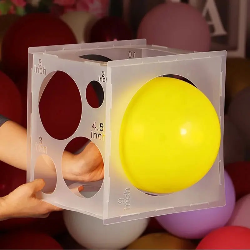 A clear plastic box with holes is shown holding a large yellow balloon for party decor.