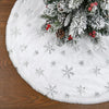 White plush Christmas tree skirt with a snowflake design resting on a wooden surface.