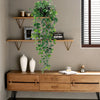 Hanging artificial plant wall decor with green foliage displayed on wooden shelves and a cabinet.
