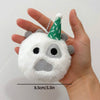 A white plush doll with gray features and a green conical hat is held in a person's hand.