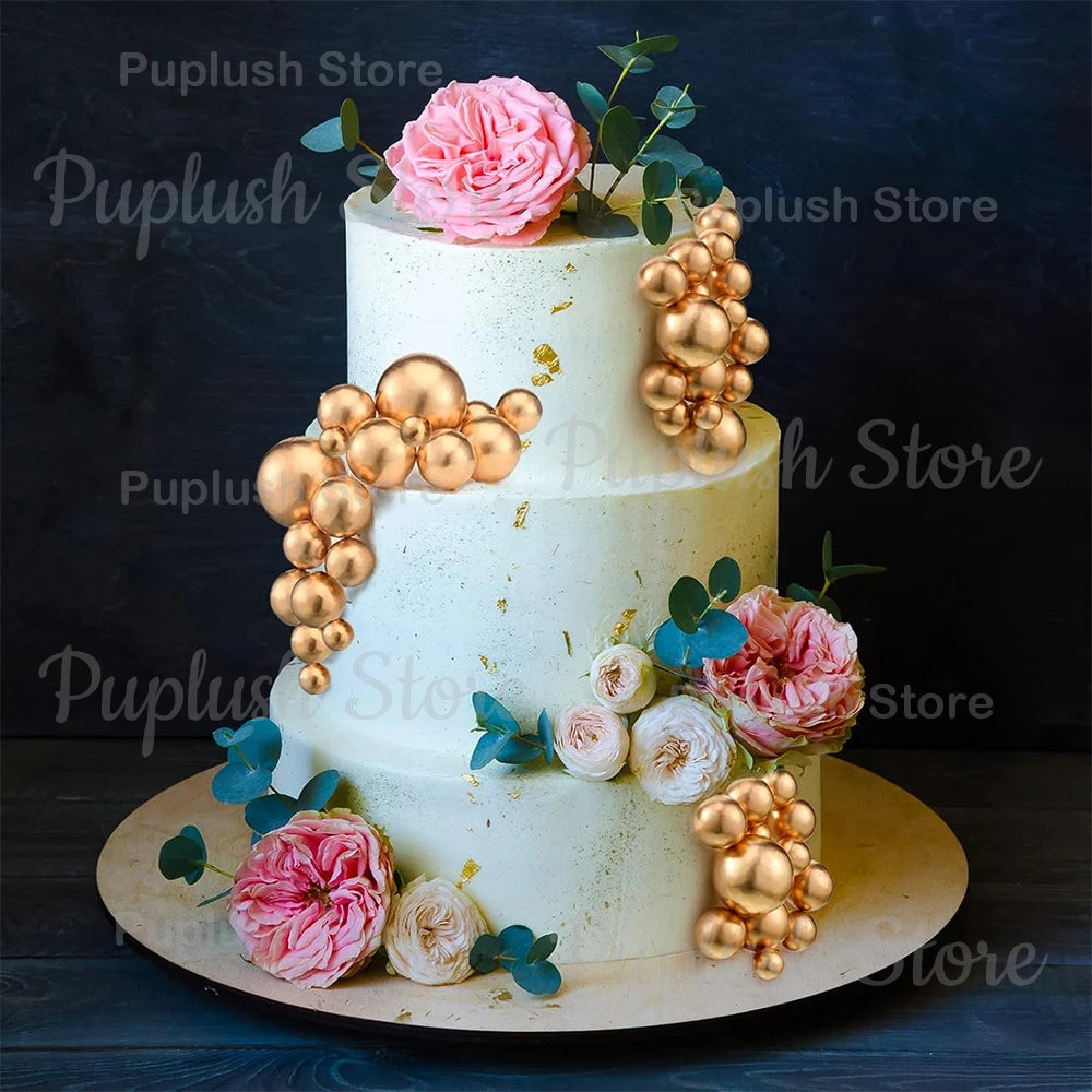 A three-tiered white cake decorated with pink roses and gold spherical accents.