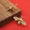 Figurine de guêpe en laiton vintage posée sur une surface en bois sur fond rouge.