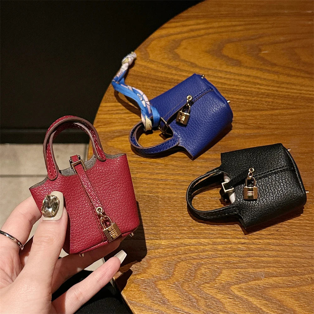 A hand holds a red mini handbag with a gold clasp and wrist strap next to a black mini handbag on a wooden table.