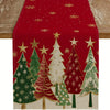 Un camino de mesa navideño festivo con un patrón de árboles de pino verdes y rojos con estrellas doradas sobre un fondo rojo.