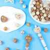 A collection of round silicone beads in various natural and pastel colors arranged on a white plate and blue background.
