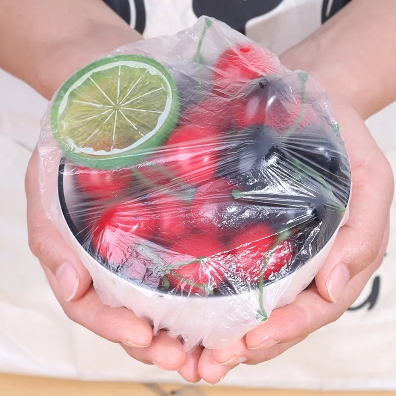 A hand holds a clear plastic wrap containing fresh red and green fruit, likely for food protection.