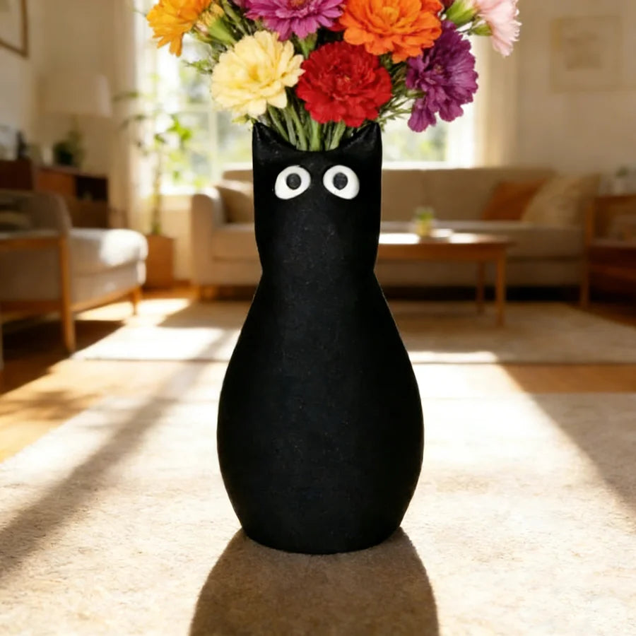 A black cat-shaped vase with white eyes filled with colorful flowers sits on a light rug.