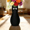 A black cat-shaped vase with white eyes filled with colorful flowers sits on a light rug.
