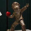 A bronze-toned resin sculpture of a child figure throwing a red heart.