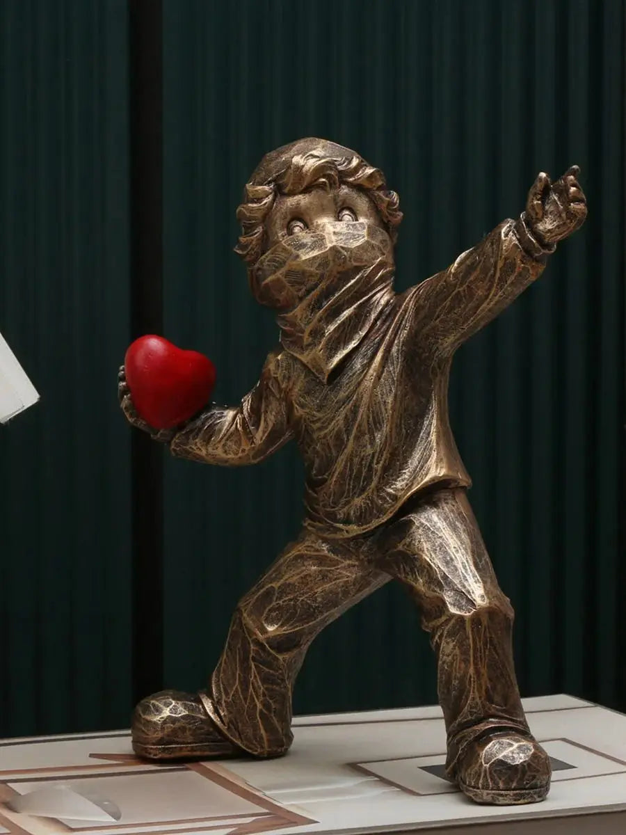 A bronze-toned resin sculpture of a child figure throwing a red heart.
