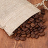 A burlap drawstring bag filled with roasted coffee beans resting on a wooden surface.