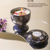 A dark ceramic bowl filled with wax and a rose-themed candle is displayed on a silver tray.