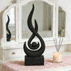 A black flame sculpture decor stands on a dark base in front of a white framed mirror.