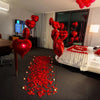 A room decorated with red heart-shaped foil balloons and a bed covered in white and red fabric.