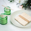 Green soy wax candles in glass jars with wooden wicks on a white plate