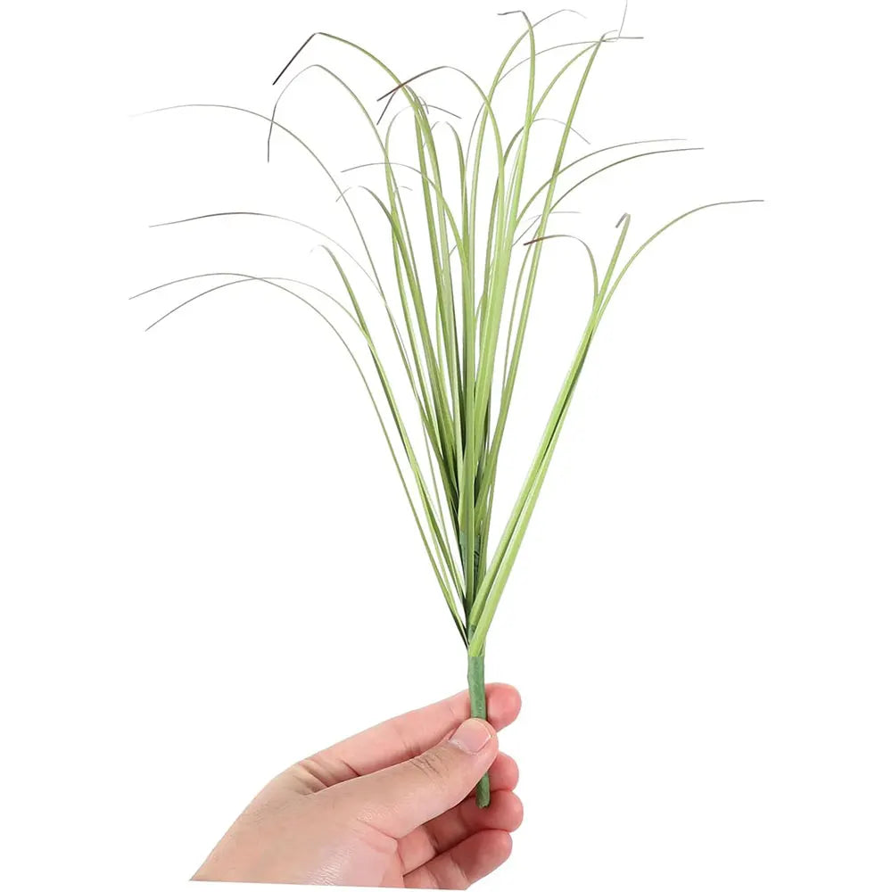 A bundle of artificial grass greenery with long, thin green blades held in a hand.