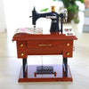 A vintage sewing machine music box with a dark body and wooden base sits on a light surface.
