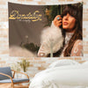 A tapestry wall hanging featuring the name Dandelion and Ella Langley above a portrait of a woman with long brown hair.