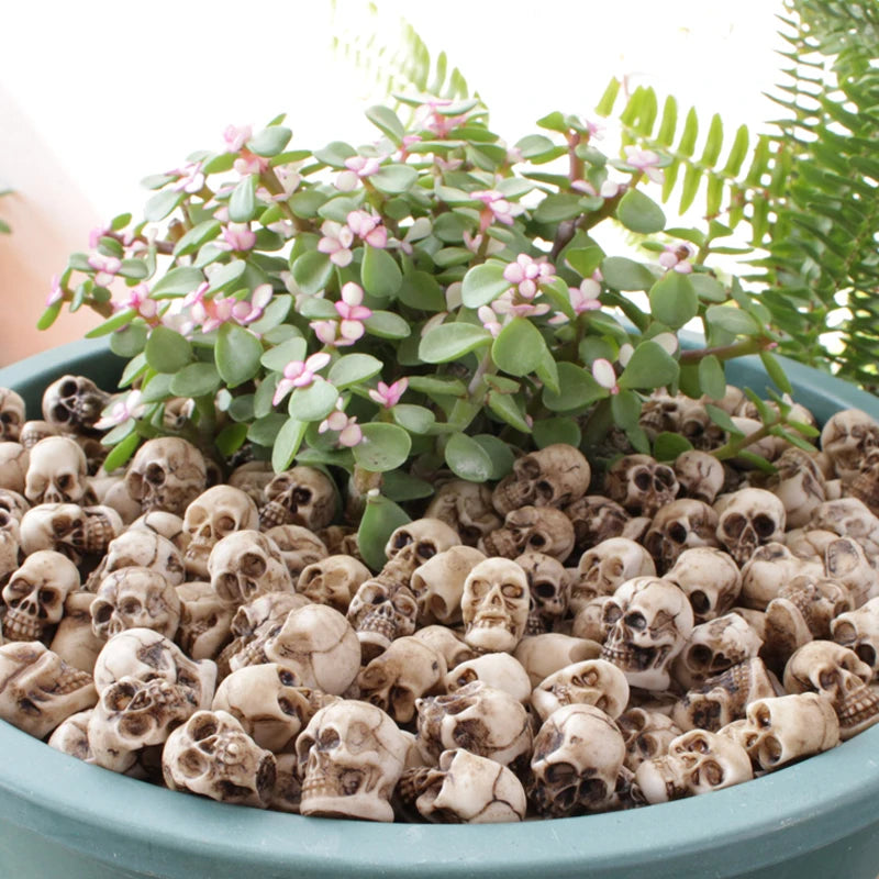 A potted plant with pink flowers sits atop a bed of realistic resin mini skulls for garden decor.
